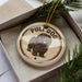 A round ornament with the text "PULL DOG" and an illustration of a shaggy dog is displayed in a box, surrounded by pine branches.