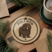 A round ornament with the text "PULI DOG" and an illustration of a shaggy dog is displayed on a wooden surface, surrounded by pine branches and a cup of coffee.