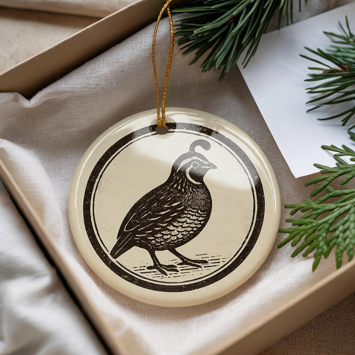 A decorative ornament featuring a black and white illustration of a bird is displayed in a box, surrounded by pine branches.