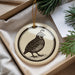 A decorative ornament featuring a black and white illustration of a bird is displayed in a box, surrounded by pine branches.