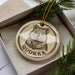 A round ornament with a picture of a wombat and the word "QUOKKA" printed on it, placed in a box with pine branches.