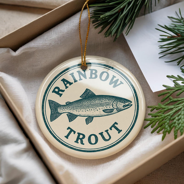A round ornament with a fish design and the text "RAINBOW TROUT" is displayed in a box with pine branches.