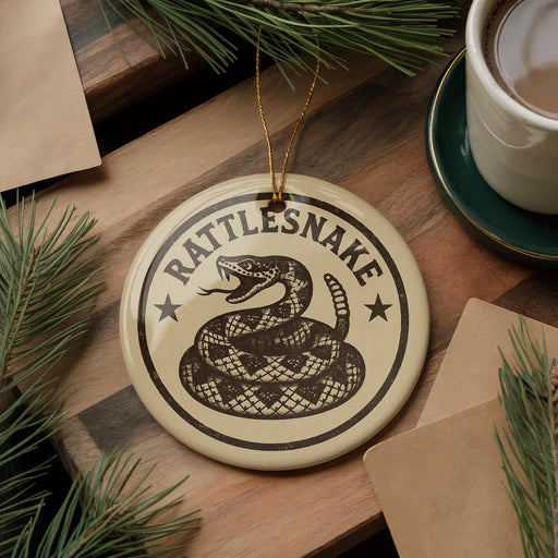 A round ornament with a snake design and the text "Rattlesnake" is displayed on a wooden surface, surrounded by pine branches and a cup of coffee.