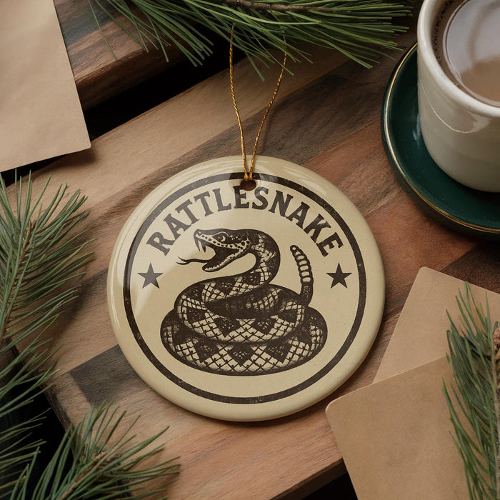 A round ornament with a snake design and the text "Rattlesnake" is displayed on a wooden surface, surrounded by pine branches and a cup of coffee.
