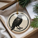 A ceramic ornament in the shape of a black bird is displayed in a box, surrounded by pine branches.