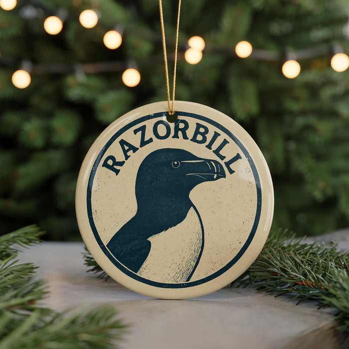 A circular ornament with the word "RAZORBILL" and a graphic of a penguin is displayed on a table, surrounded by pine branches and twinkling lights.