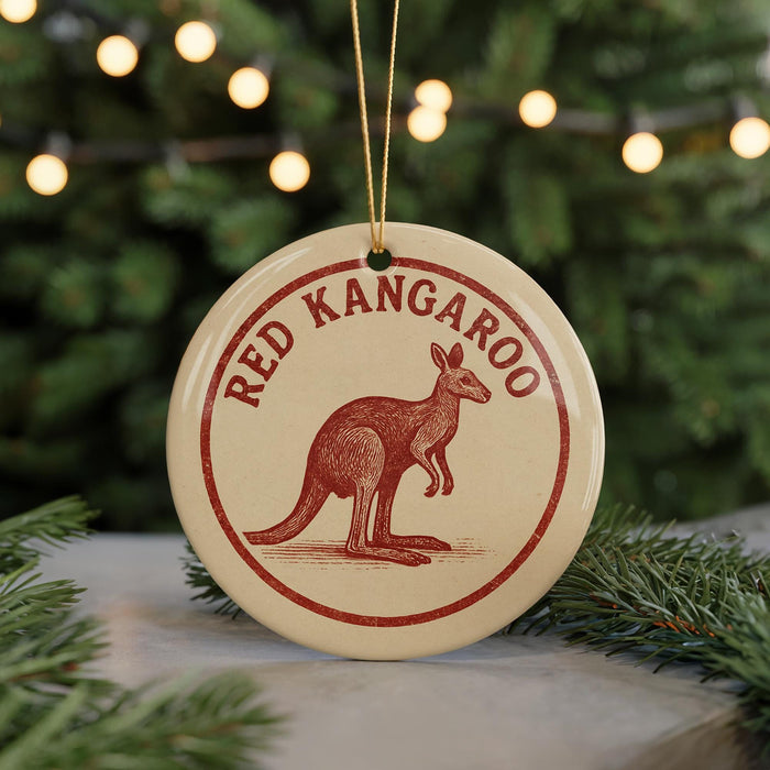 A round ornament with the text "RED KANGAROO" and an illustration of a kangaroo is displayed on a table, with a blurred background of a Christmas tree.