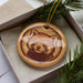 A ceramic ornament in the shape of a red panda, with a brown and beige color scheme, is displayed in a box surrounded by pine branches.