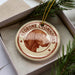 A circular ornament with a brown dog's head and the text "REDBONE COONHOUND" printed on it, placed inside a box with pine branches.