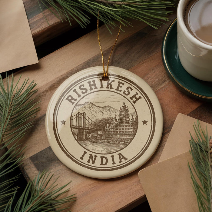 A decorative ornament with the text "RISHKESH INDIA" and an illustration of a bridge is displayed on a wooden surface, surrounded by pine branches and a cup of coffee.