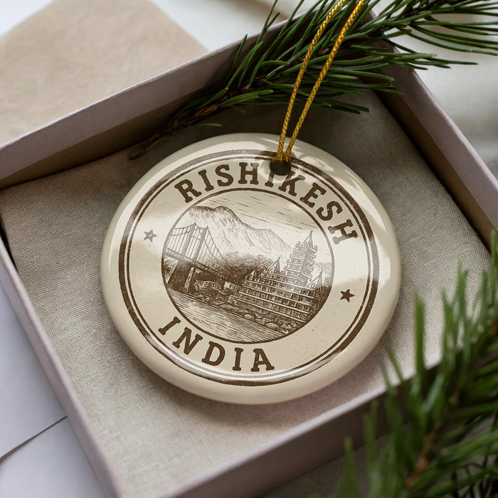 A decorative ornament with the text "RISHKESH INDIA" printed on it, surrounded by a pine branch and placed in a box.