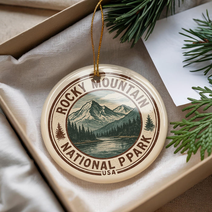 A round ornament with a mountain landscape and pine trees, featuring the text "ROCKY MOUNTAIN NATIONAL PARK USA".