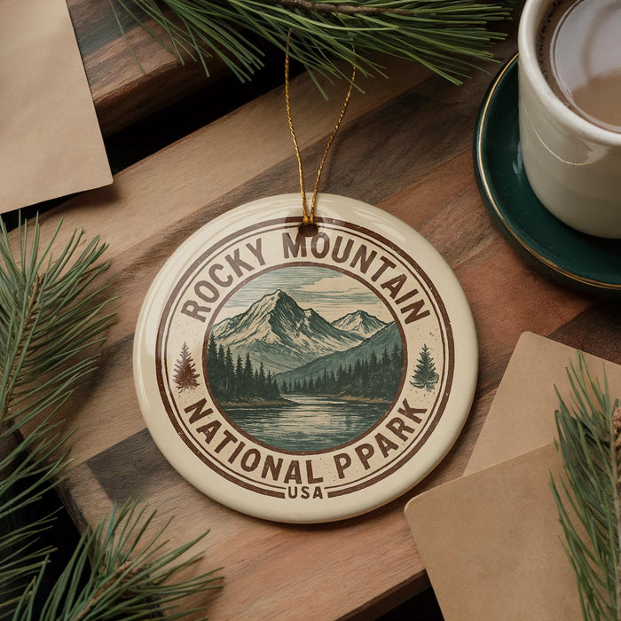 A decorative ornament featuring the Rocky Mountain National Park logo, surrounded by pine branches and a cup of coffee on a wooden surface.
