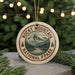 A round ornament with a mountain landscape and pine trees, featuring the text "ROCKY MOUNTAIN NATIONAL PARK USA" on it, is hanging from a string.