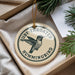 A round ornament with a hummingbird design, hanging from a string, placed inside a box with pine branches.