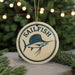 A round ornament with the word "SAILFISH" and a graphic of a sailfish is displayed in front of a Christmas tree with twinkling lights.