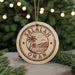 A circular ornament with the text "SALALAH OMAN" printed on it, surrounded by a palm tree and mountains, is hanging from a string in front of a Christmas tree with lights.