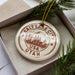 A circular ornament with the text "Salt Lake City USA Utah" printed on it, placed inside a box with pine branches.