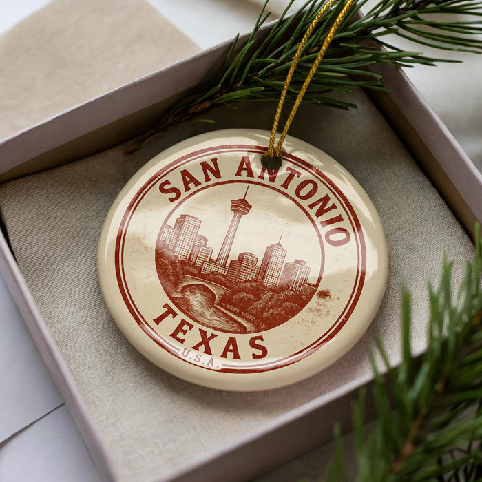 A circular ornament with the text "SAN ANTONIO TEXAS" and a graphic of the city of San Antonio, Texas, is displayed in a box with pine branches.