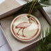 A ceramic ornament in the shape of a bird, possibly a crane, is displayed in a box with pine branches.