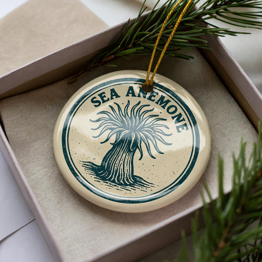 A decorative ornament in a box, featuring a circular design with a stylized tree or plant motif and the text "SEA ANEMONE" printed on it.