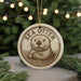 A round ornament featuring a sea otter, with the text "SEA OTTER" printed on it, is displayed in front of a blurred background with Christmas lights.
