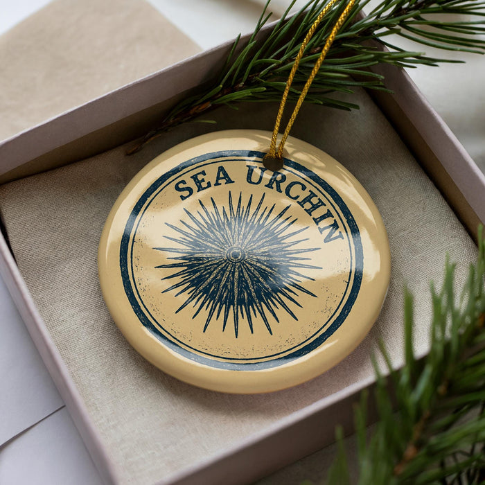 A decorative ornament with the text "SEA URCHIN" on it, placed in a box with pine branches.