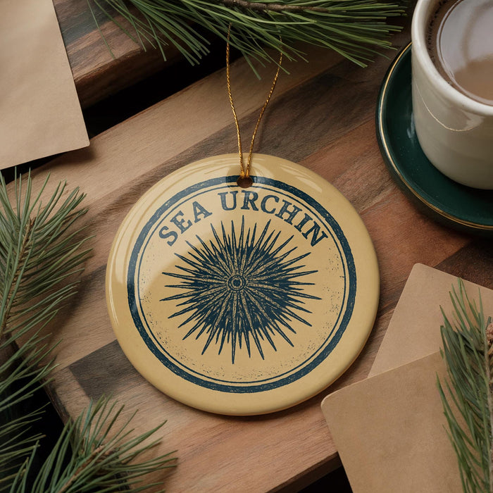 a round ornament with a blue and yellow design, hanging on a wooden surface. The ornament has the text "SEA URCHIN" written on it.