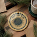 a round ornament with a blue and yellow design, hanging on a wooden surface. The ornament has the text "SEA URCHIN" written on it.