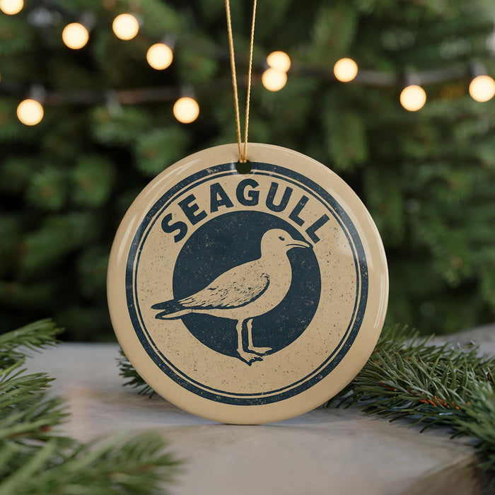 A round ornament with the word "SEAGULL" and a graphic of a seagull is displayed on a table, surrounded by pine branches and twinkling lights.