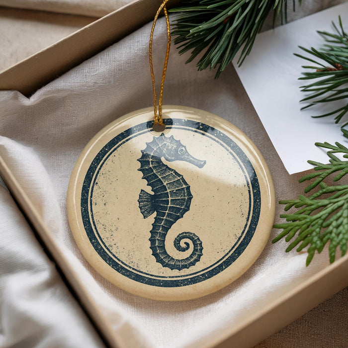 A round ornament featuring a seahorse design is displayed in a box, surrounded by pine branches.
