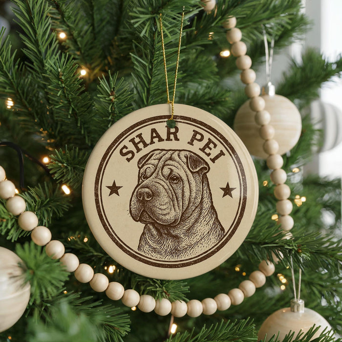 A circular ornament with a brown and white design hangs from a Christmas tree, featuring a dog's face and the text "SHAR PEI".