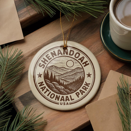 A circular ornament with the text "Shenandoah National Park" and a mountain landscape design hangs on a wooden surface, surrounded by pine branches and a cup of coffee.