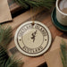 A circular ornament with the text "SHETLAND ISLANDS SCOTLAND" printed on it, surrounded by pine branches and a cup of coffee on a wooden surface.