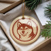 A round ornament with a picture of a dog's face is displayed in a box, surrounded by pine branches.