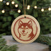 A round ornament featuring a dog's face is displayed in front of a Christmas tree with twinkling lights.