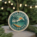 A circular ornament with the text "SIARGAO PHILIPPINES" and a tropical beach scene, featuring palm trees and a sunset, is displayed in front of a Christmas tree with lights.