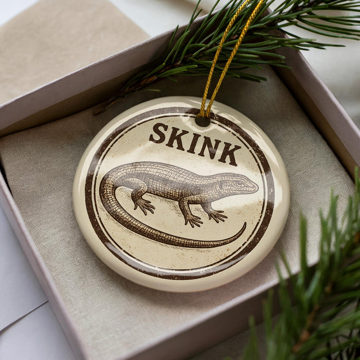 A ceramic ornament in a box, featuring a detailed illustration of a lizard or salamander.