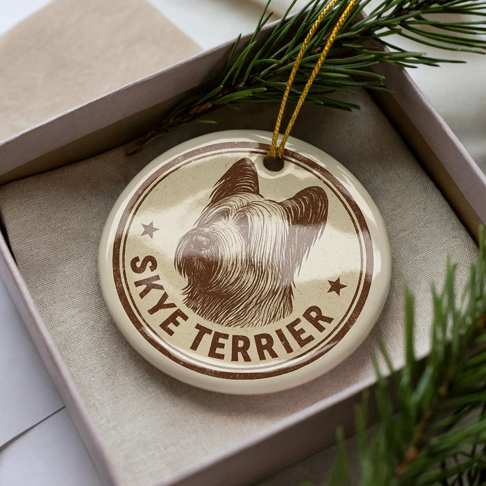 A circular ornament featuring a Skye Terrier dog's head, with the text "SKYE TERRIER" printed on it, is displayed in a box surrounded by pine branches.