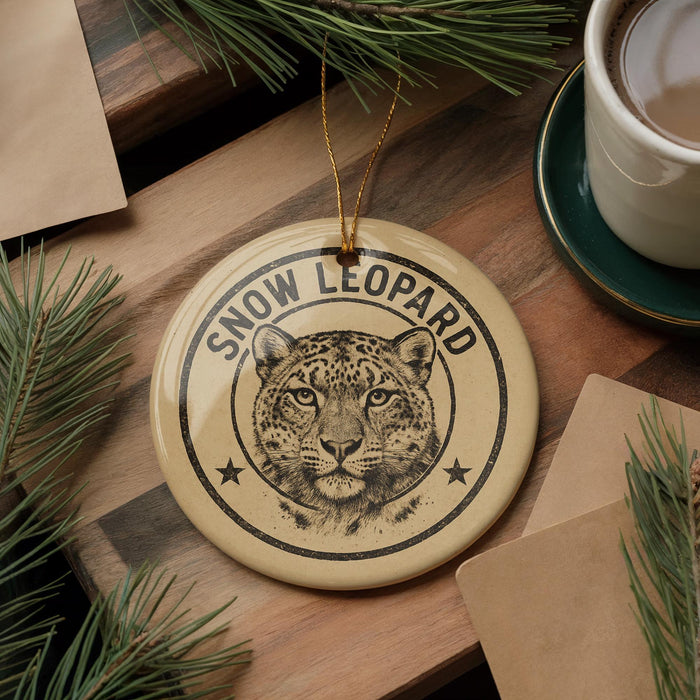A round ornament featuring a leopard's face is displayed on a wooden surface, surrounded by pine branches and a cup of coffee.
