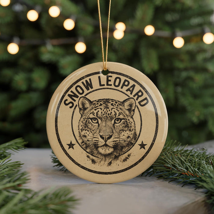 A round ornament with a leopard's face and the text "SNOW LEOPARD" printed on it, hanging from a string.