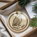A round ornament with a picture of a snowy owl on it, hanging from a string.