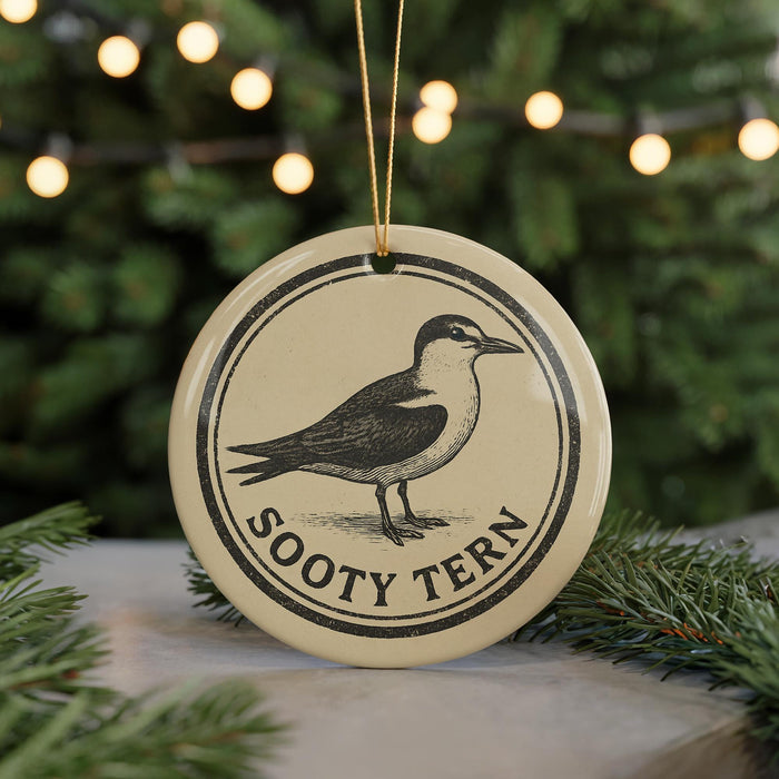 A round ornament with a bird image and the text "Sooty Tern" on it, hanging in front of a Christmas tree with twinkling lights.