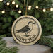 A round ornament with a bird image and the text "Sooty Tern" on it, hanging in front of a Christmas tree with twinkling lights.