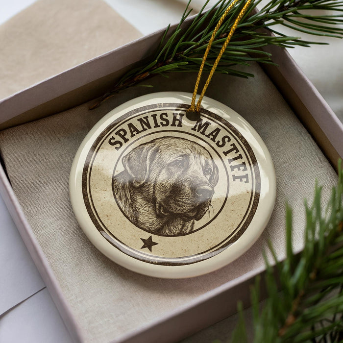 A decorative ornament featuring a dog's face, specifically a Spanish mastiff, is displayed in a box with pine branches.