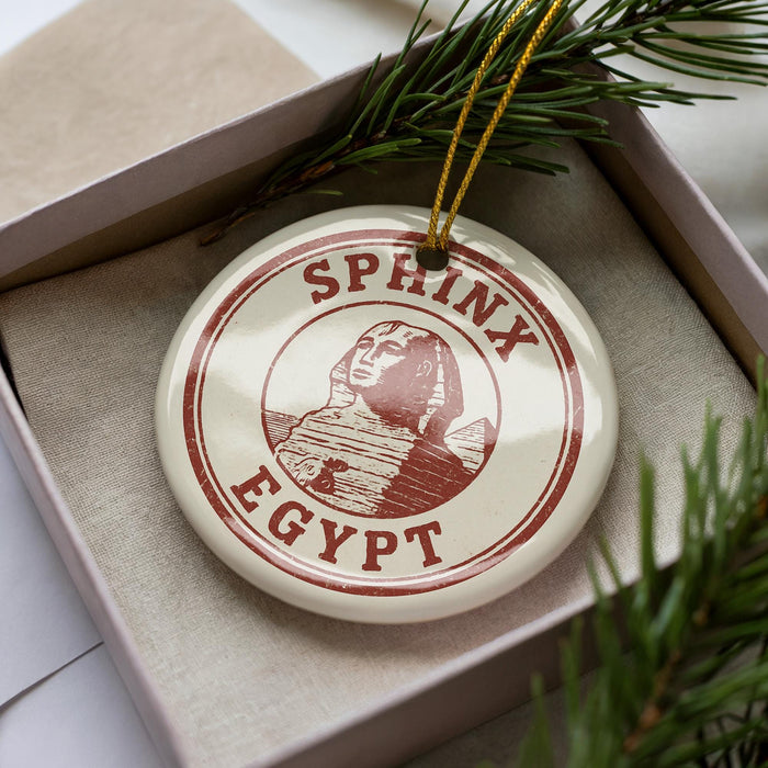 A circular ornament with the text "SPHINX EGYPT" printed on it, surrounded by a pine branch.