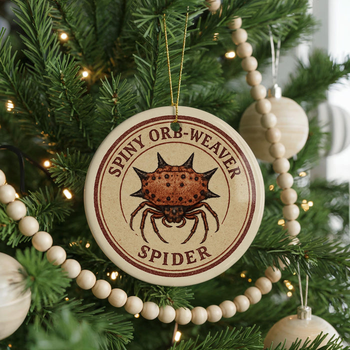 A Christmas tree decorated with ornaments, including a round ornament with a spider image and the text "SPINNY ORB-WEAVER SPIDER".
