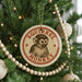 A round ornament with a monkey image is hanging on a Christmas tree, surrounded by other ornaments and lights.
