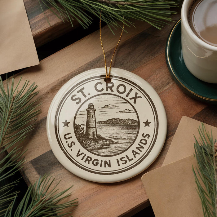 A circular ornament with the text "ST. CROIX U.S. VIRGIN ISLANDS" and a lighthouse illustration is displayed on a wooden surface, surrounded by pine branches and a cup of coffee.