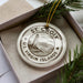 A white ornament with a lighthouse and mountains, labeled "St. Croix, U.S. Virgin Islands", is displayed in a box with pine branches.